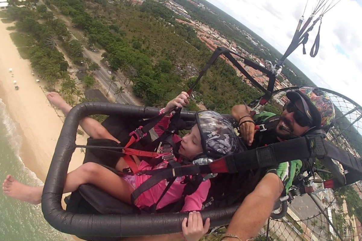 Criança voando de paramotor com piloto sobre a orla