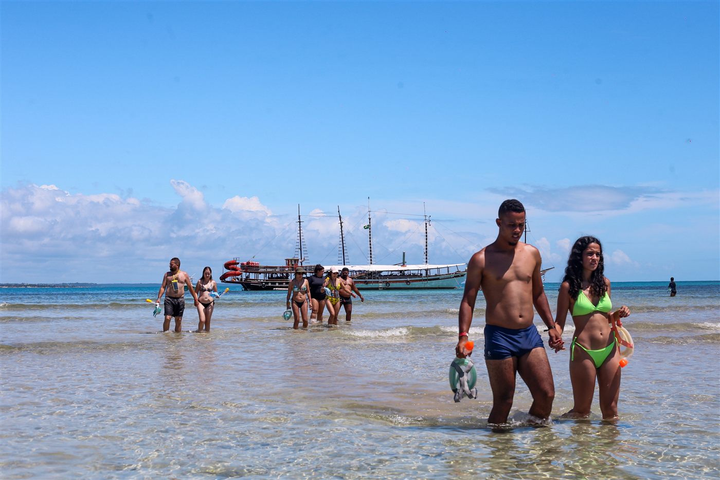Visitantes de snorkel nas piscinas naturais do Recife de Fora com escuna ao fundo
