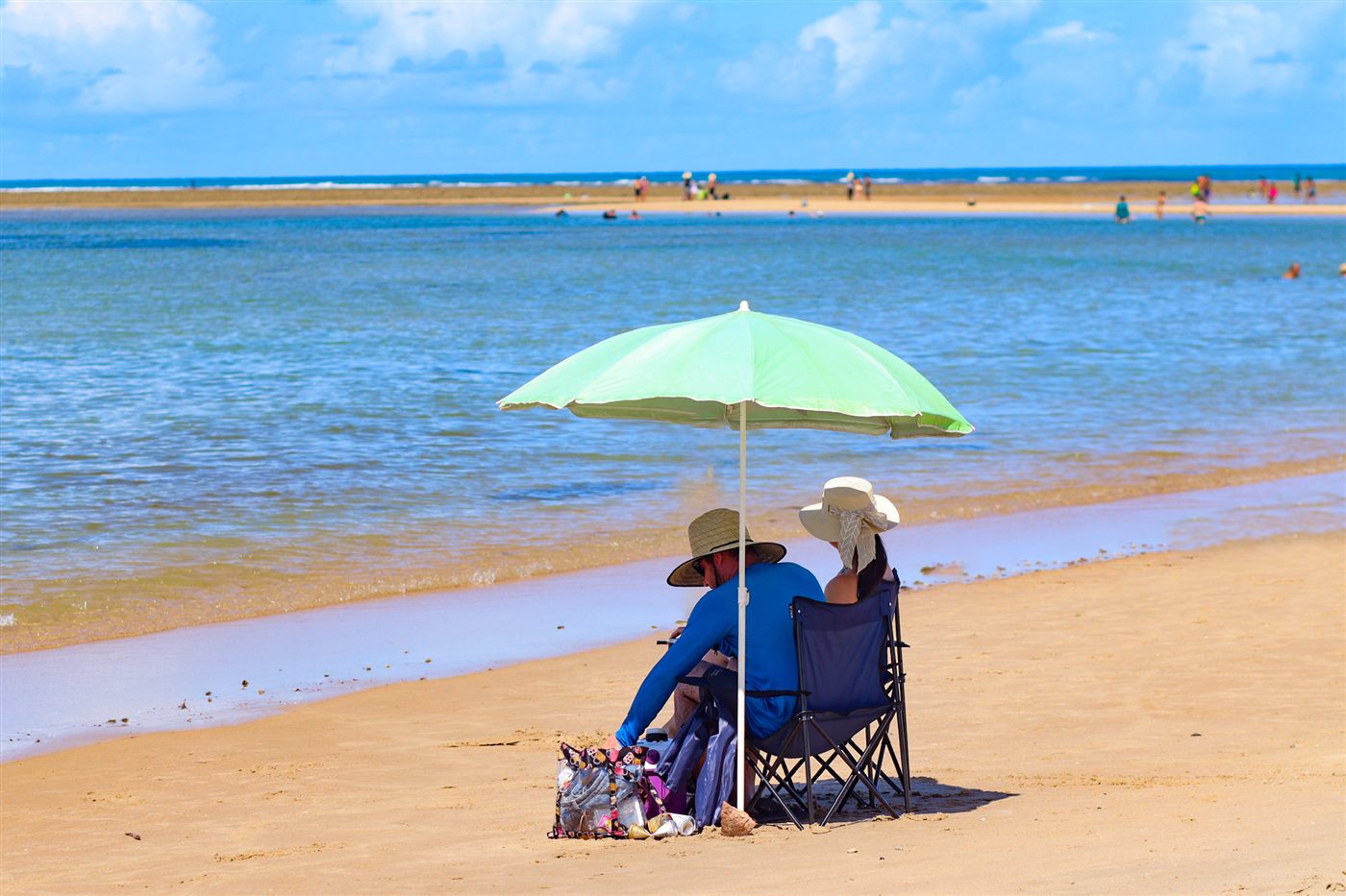Casal sob guarda-sol observando o mar calmo em praia da região
