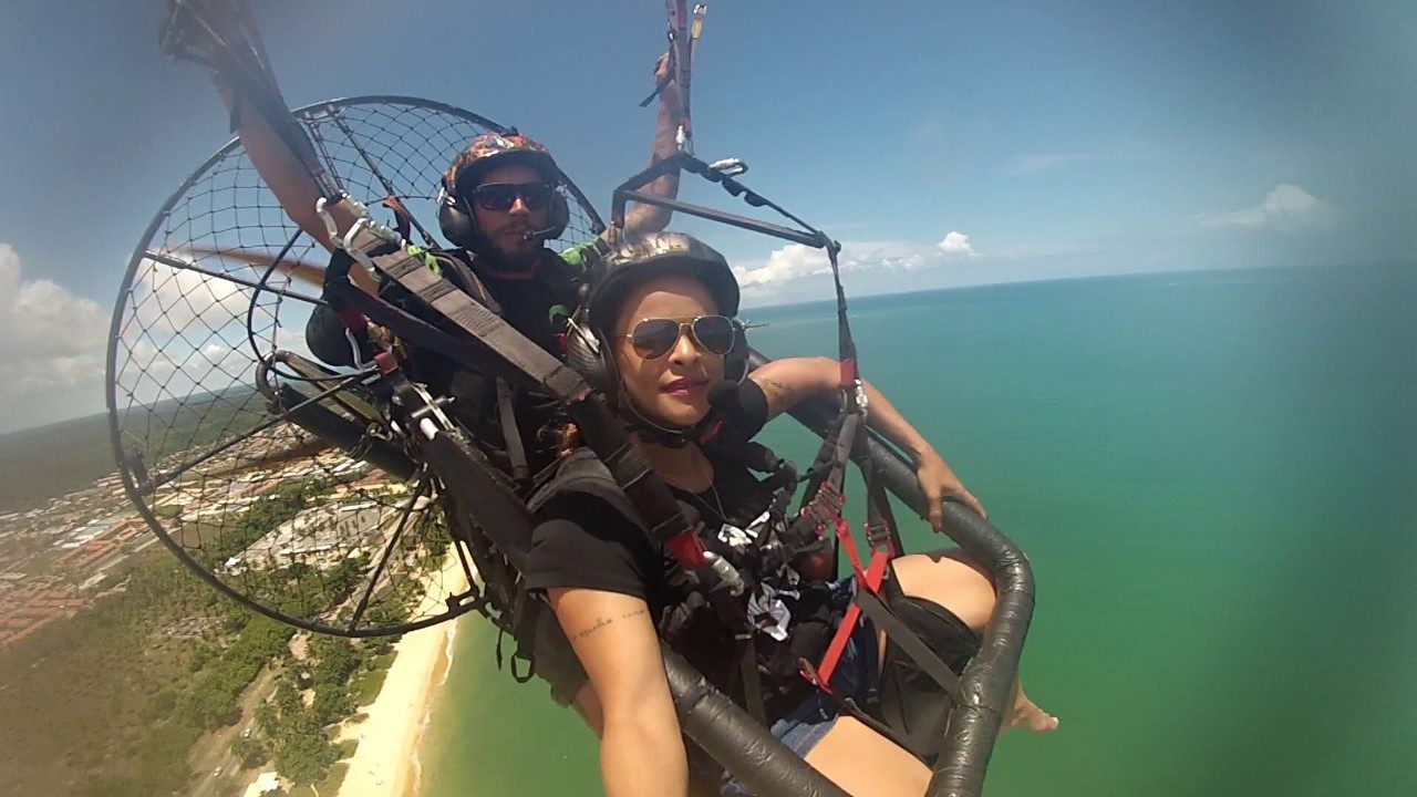 Dupla voando de paramotor sobre o mar esverdeado da orla de Porto Seguro